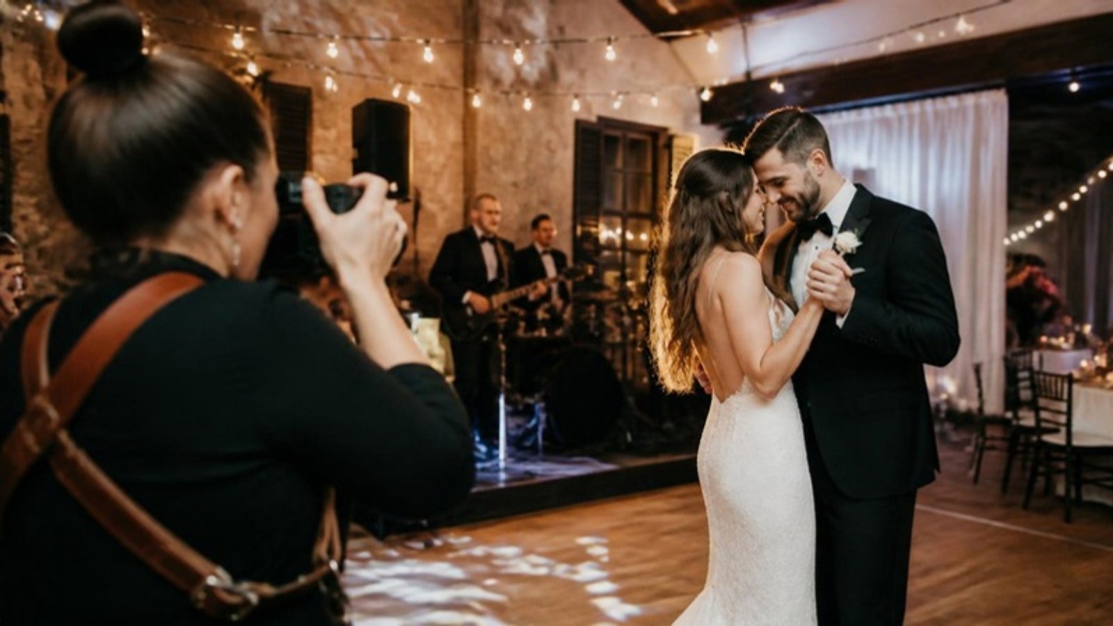Fotógrafa registrando os noivos dançando enquanto uma banda toca ao fundo em uma recepção de casamento